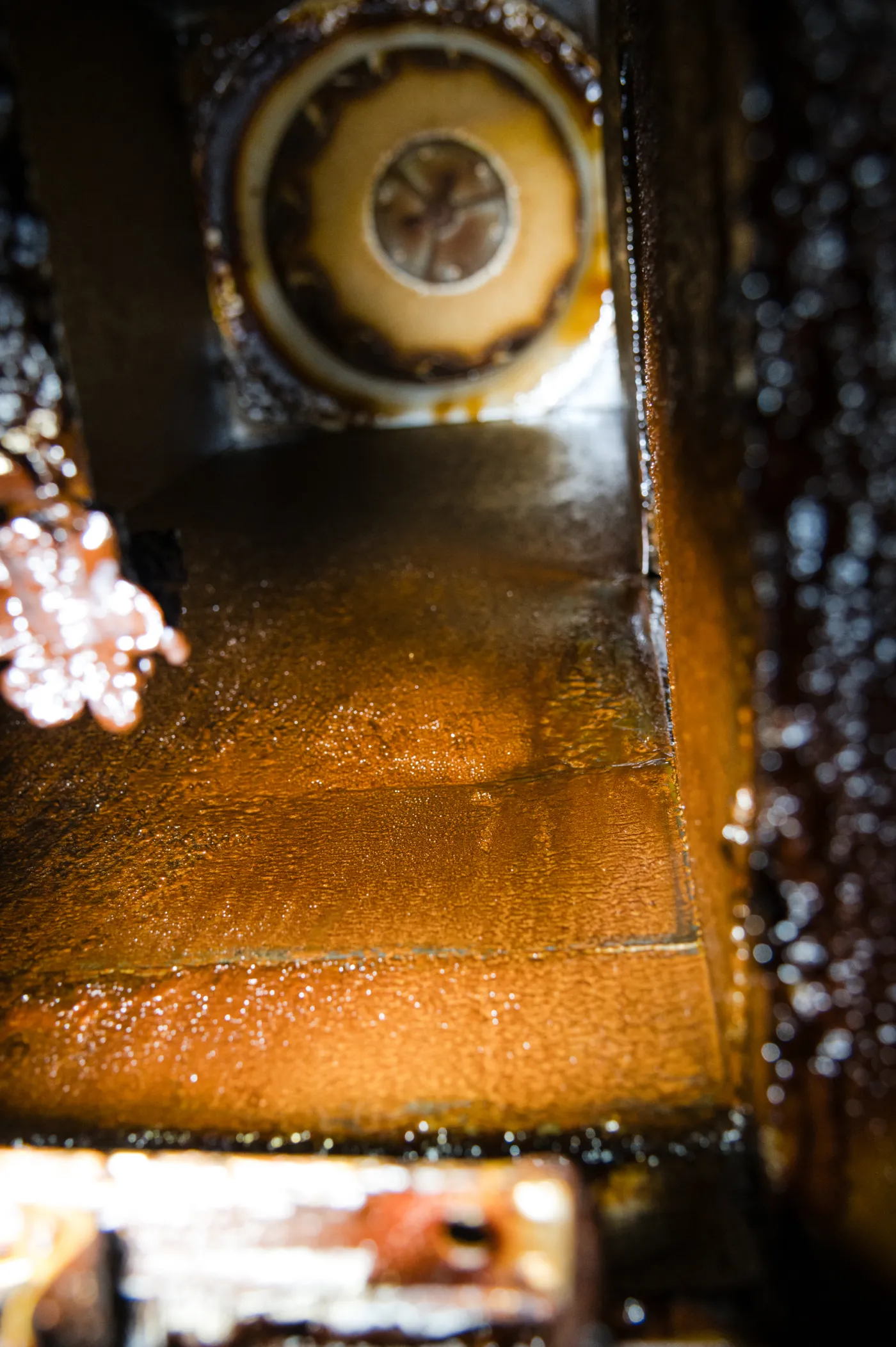 grease-1 Inside of a greasy, industrial metal vent or duct with brown residue coating the surfaces.