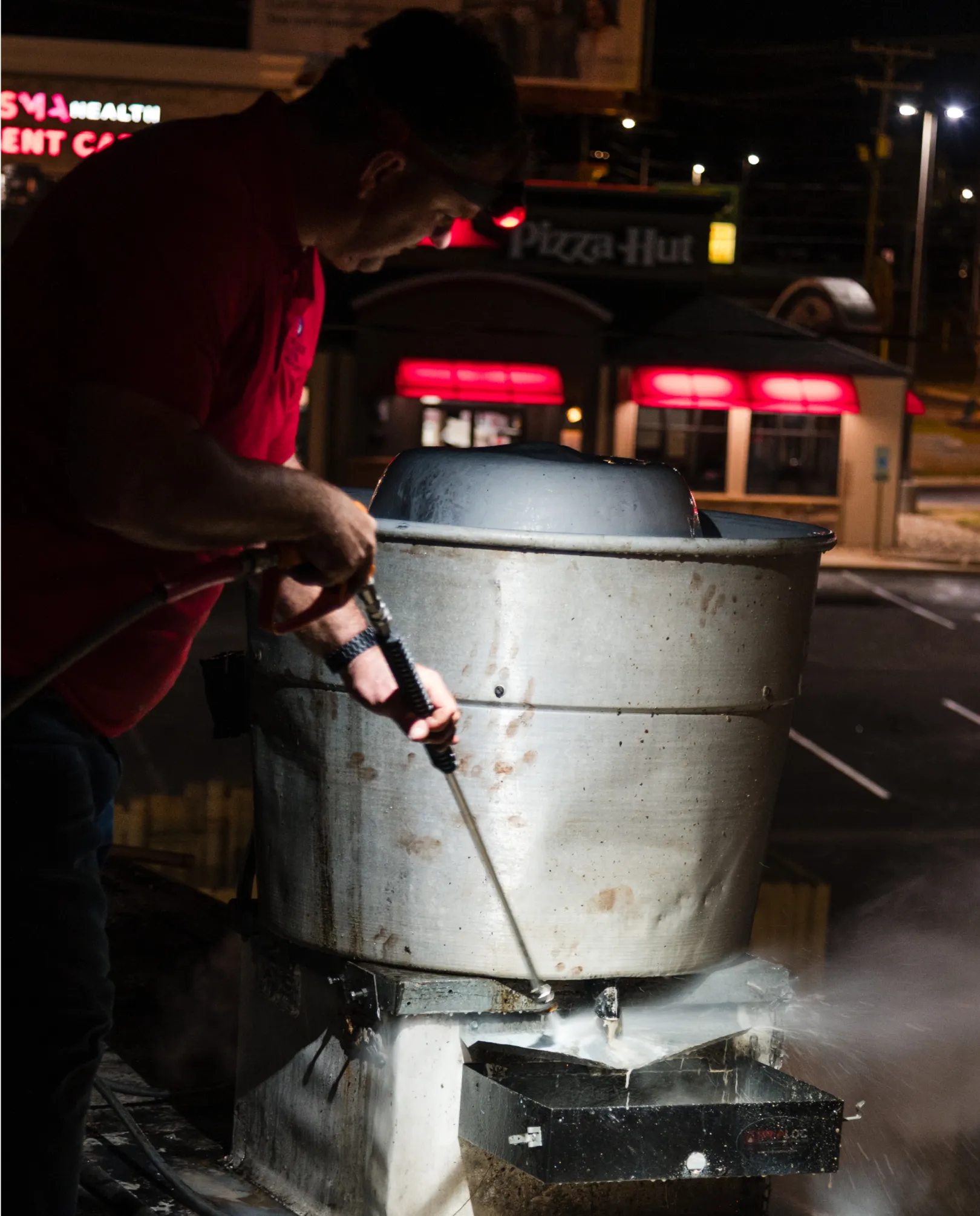 grease-3 Person power washing a large metal vent on a rooftop at night, with a Pizza Hut in the background.